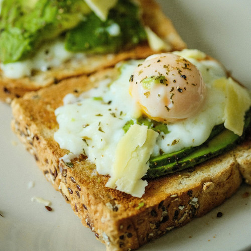 Poached egg on avocado toast with multigrain bread, topped with herbs and seasonings on white plate