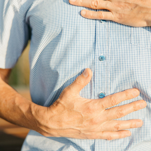 Person holding their abdomen area with both hands over blue and white striped shirt, indicating digestive discomfort
