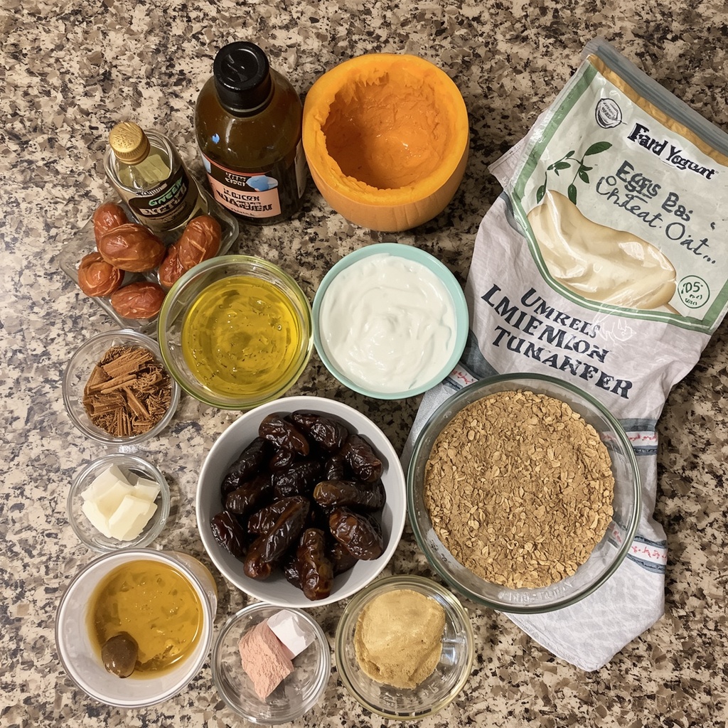 àIngrédients des muffins citrouille et dattes disposés sur un plan de travail : purée de citrouille, œufs, yaourt grec, huile d'olive, dattes, miel, farine de blé entier, flocons d'avoine et épices