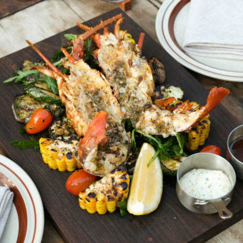 Demi-homards grillés avec marques de gril dorées, herbes fraîches et quartiers de citron sur une poêle en fonte